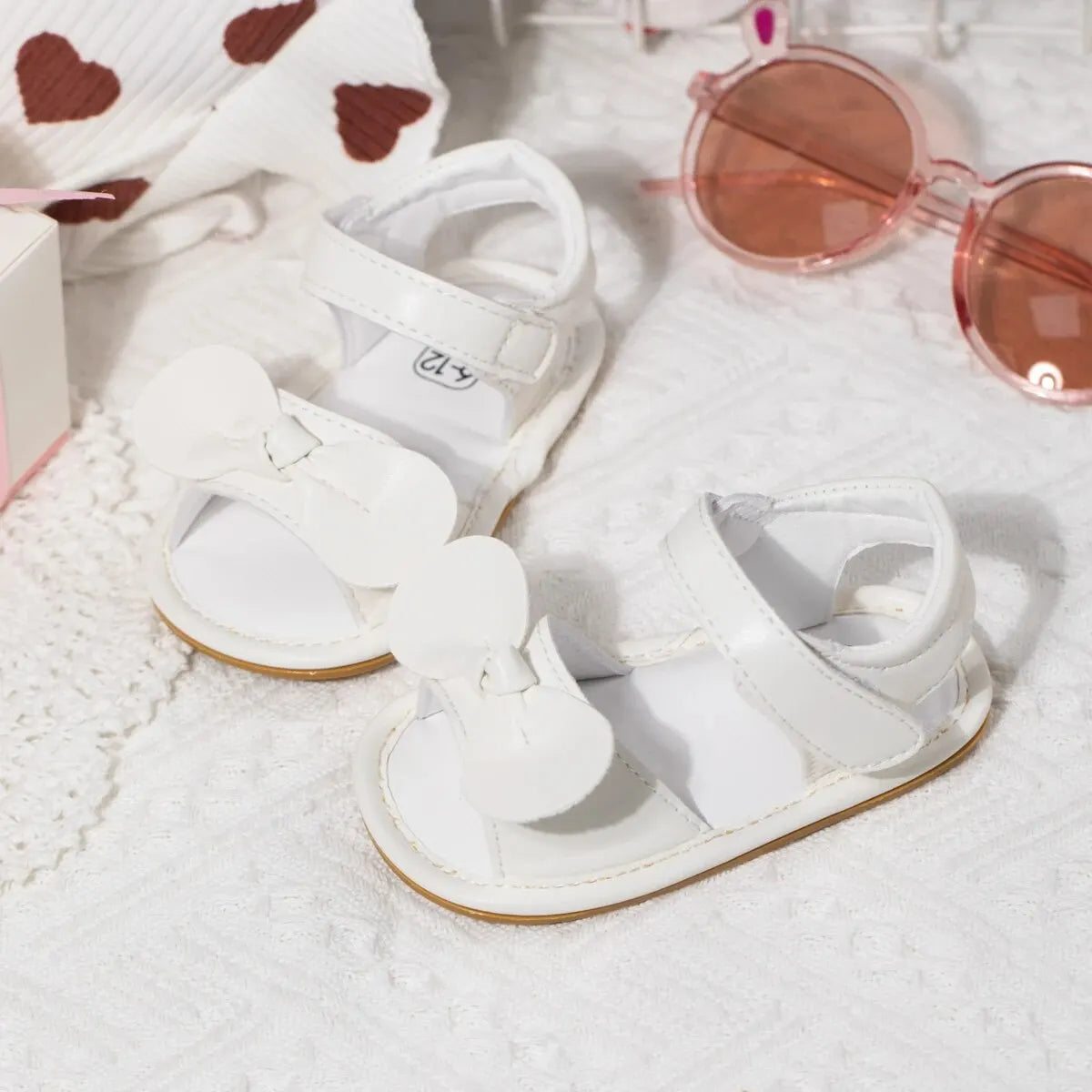 White sandals with a heart-patterned sweater and pink sunglasses on a white background