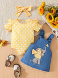 Yellow polka dot baby romper, blue denim dress with elephant design, and yellow headband on a wooden surface with flowers.