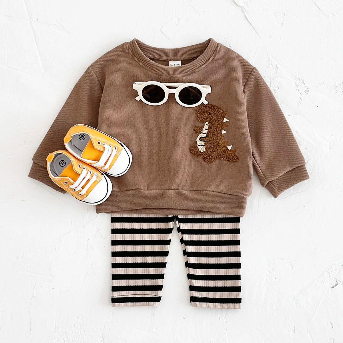 Children's outfit with brown sweatshirt, striped pants, and shoes on a white background