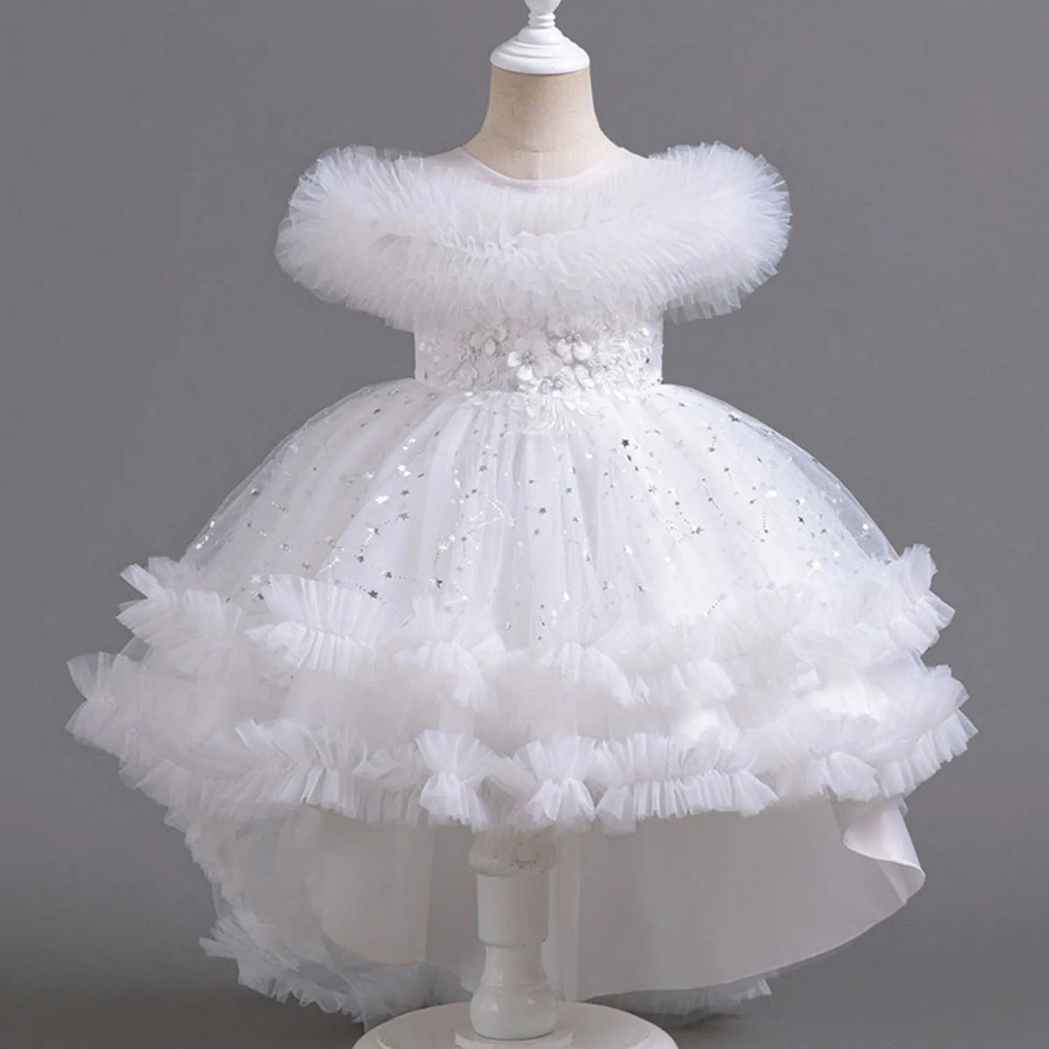 White children's dress with floral details on a mannequin against a gray background