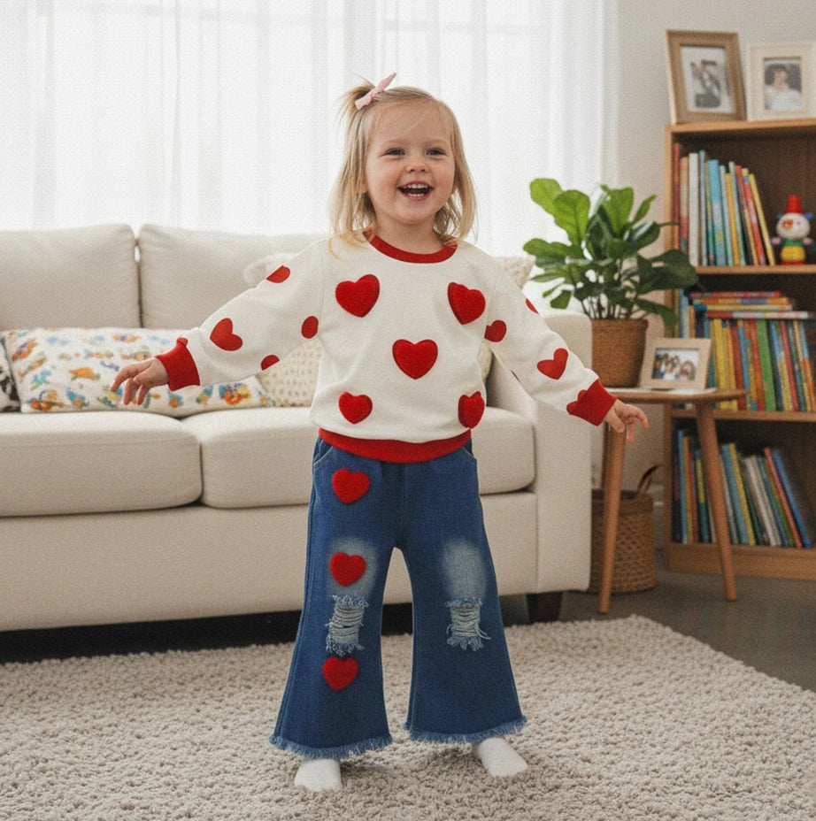 Child wearing a sweater with red heart patterns in a living room.