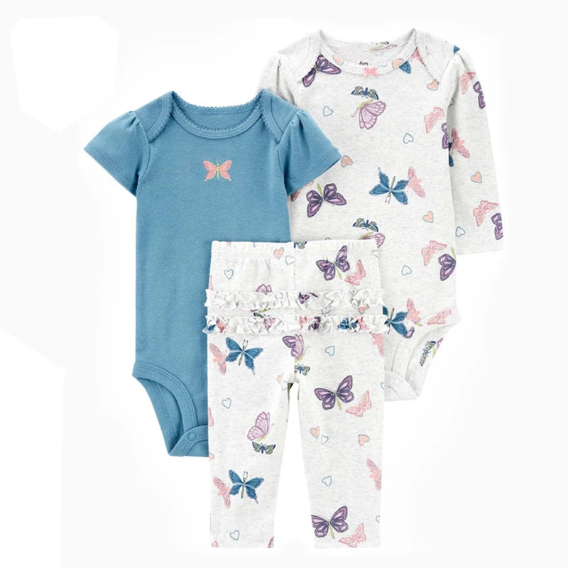 Set of baby clothing with blue bodysuit, white shirt with butterfly pattern, and white pants with butterfly pattern on a white background.