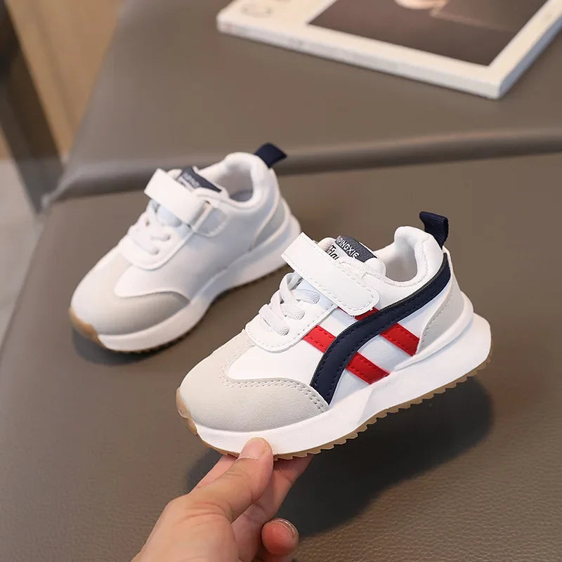 White sneakers with red and blue stripes held by a hand on a gray surface.