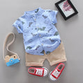 Children's outfit with blue shirt and beige shorts, red sneakers, and a toy camera on a gray surface.