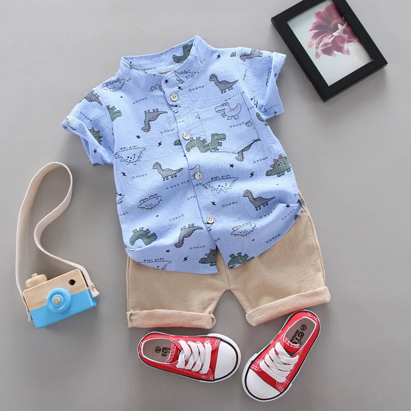 Children's outfit with blue shirt and beige shorts, red sneakers, and a toy camera on a gray surface.