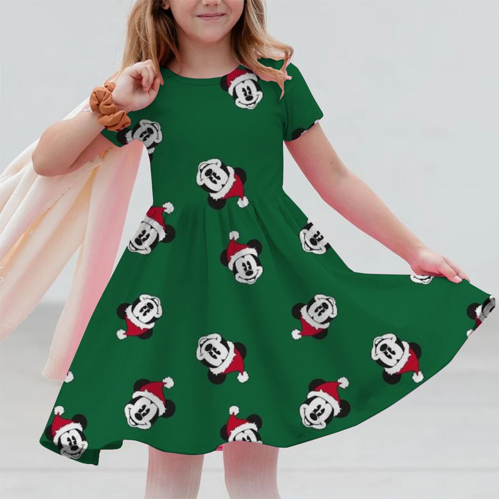 Child wearing a green dress with festive Mickey Mouse pattern on a plain background