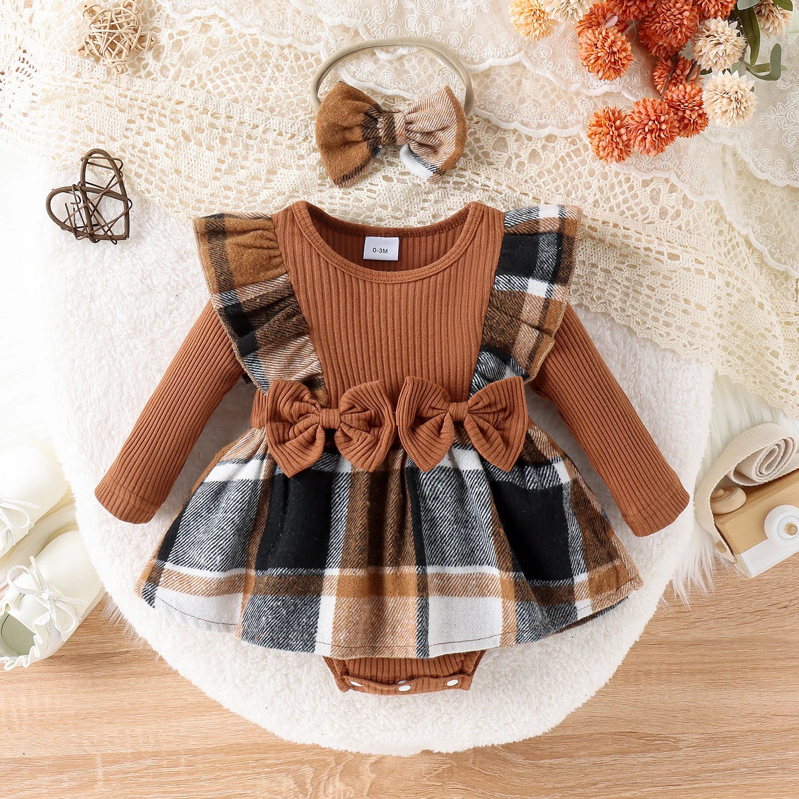 Baby outfit with plaid dress and brown long-sleeve top on a textured surface