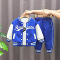 Children's blue and white jacket and pants set on hangers against a gray curtain background.
