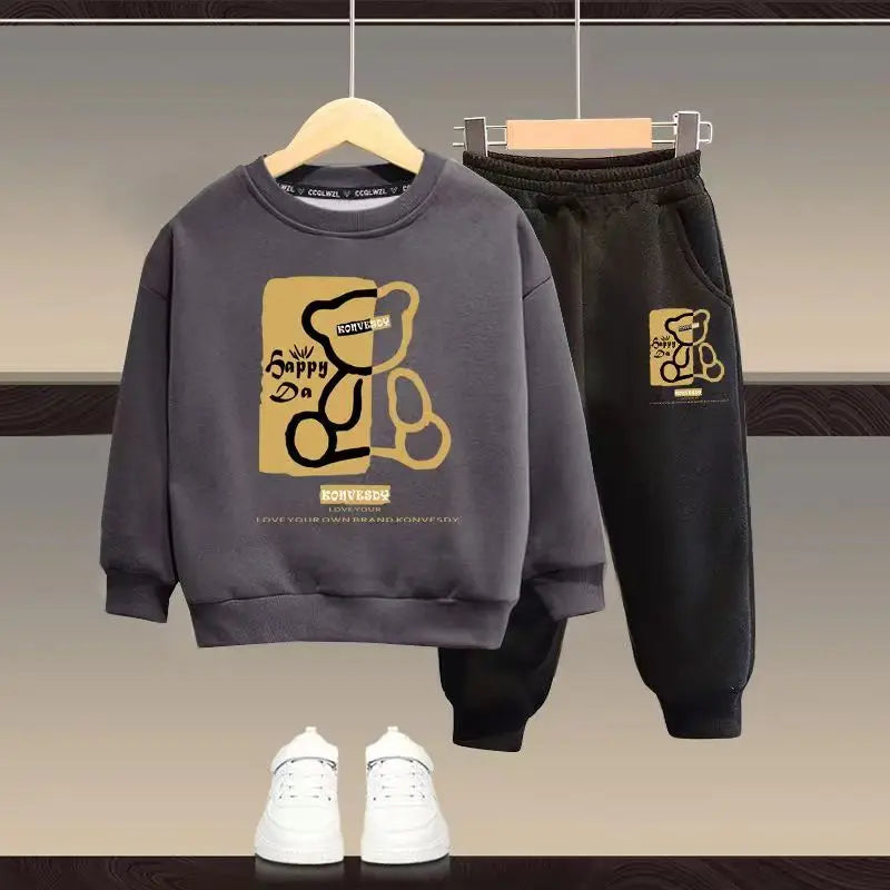 Children's gray sweatshirt and black pants with a logo, paired with white sneakers on a neutral background.