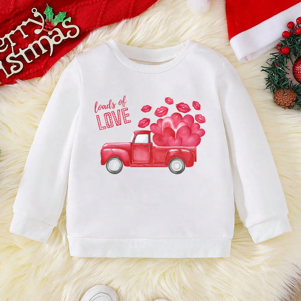 White sweatshirt with a red truck and heart design on a textured surface with Christmas decorations.