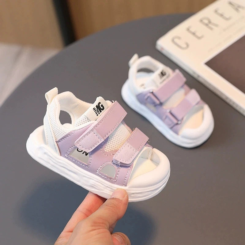 White and purple children's sandals held by a hand on a dark surface.