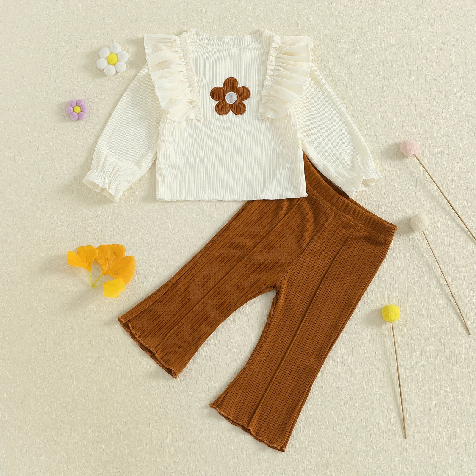 White blouse with flower design and brown pants on a beige background