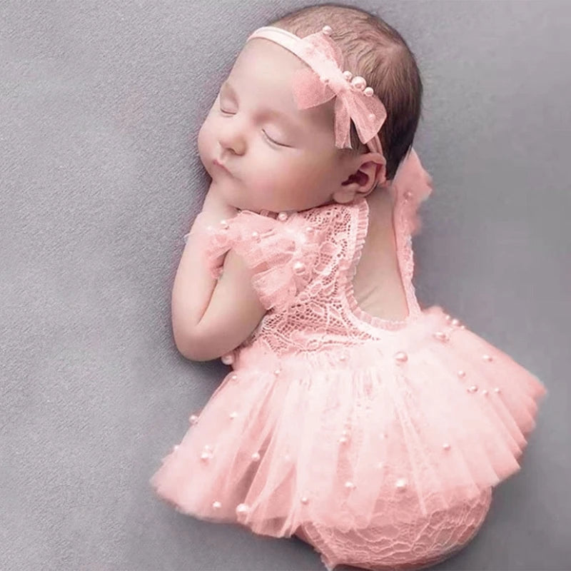 Newborn baby in a pink lace outfit with a matching headband on a gray background