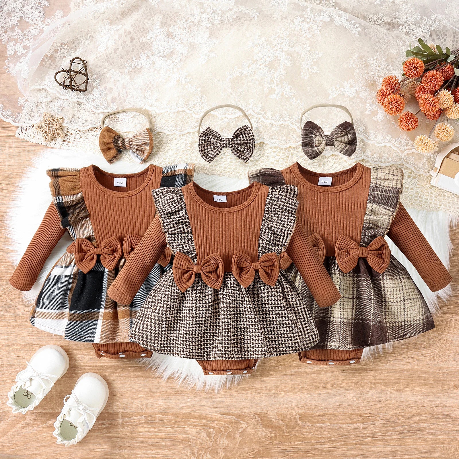 Three baby outfits with plaid skirts and brown tops on a wooden surface, accompanied by hair bows and shoes.