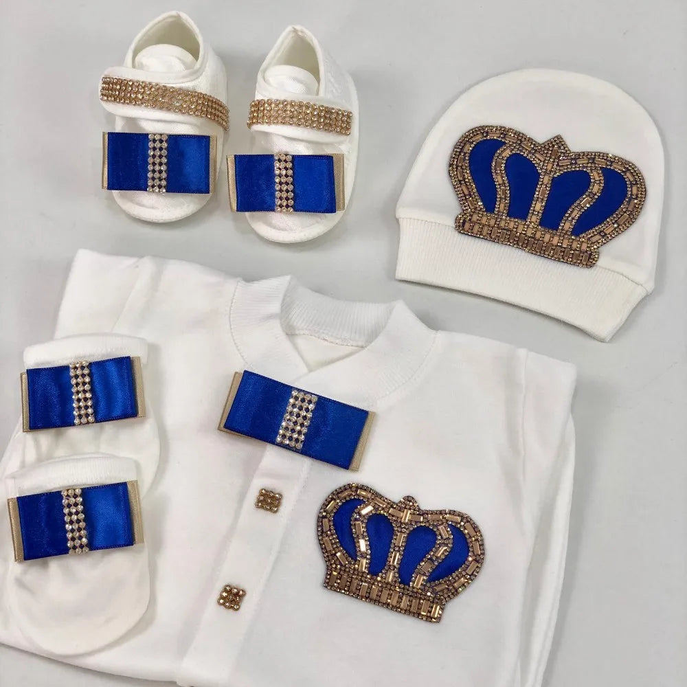 Baby outfit set with white shirt, pants, socks, and hat featuring blue and gold crowns on a light gray background.