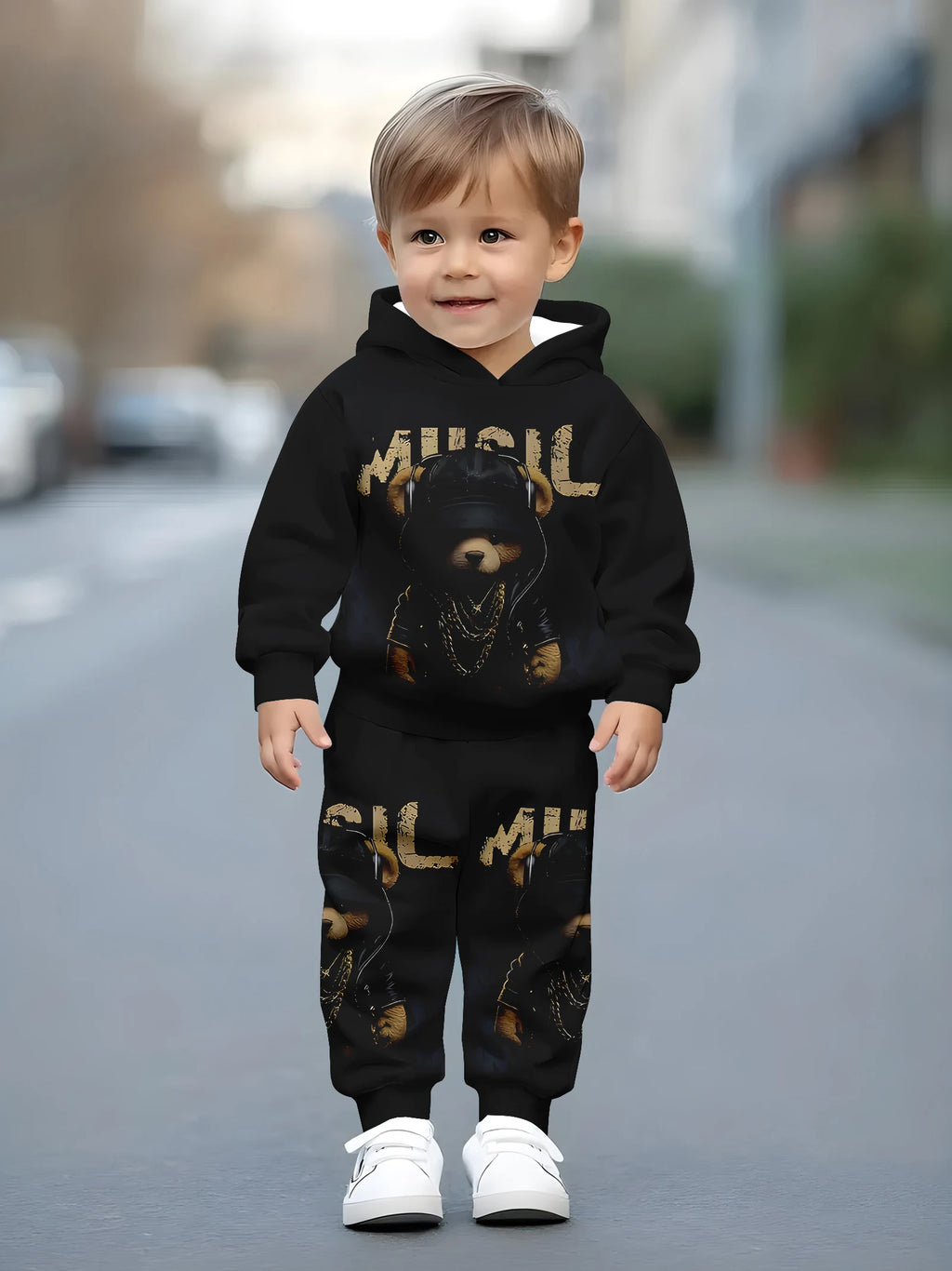 Child wearing a black hoodie and pants with gold text and graphics, standing on a street.