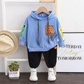 Children's blue hoodie with text design on a hanger, black pants, and white sneakers.