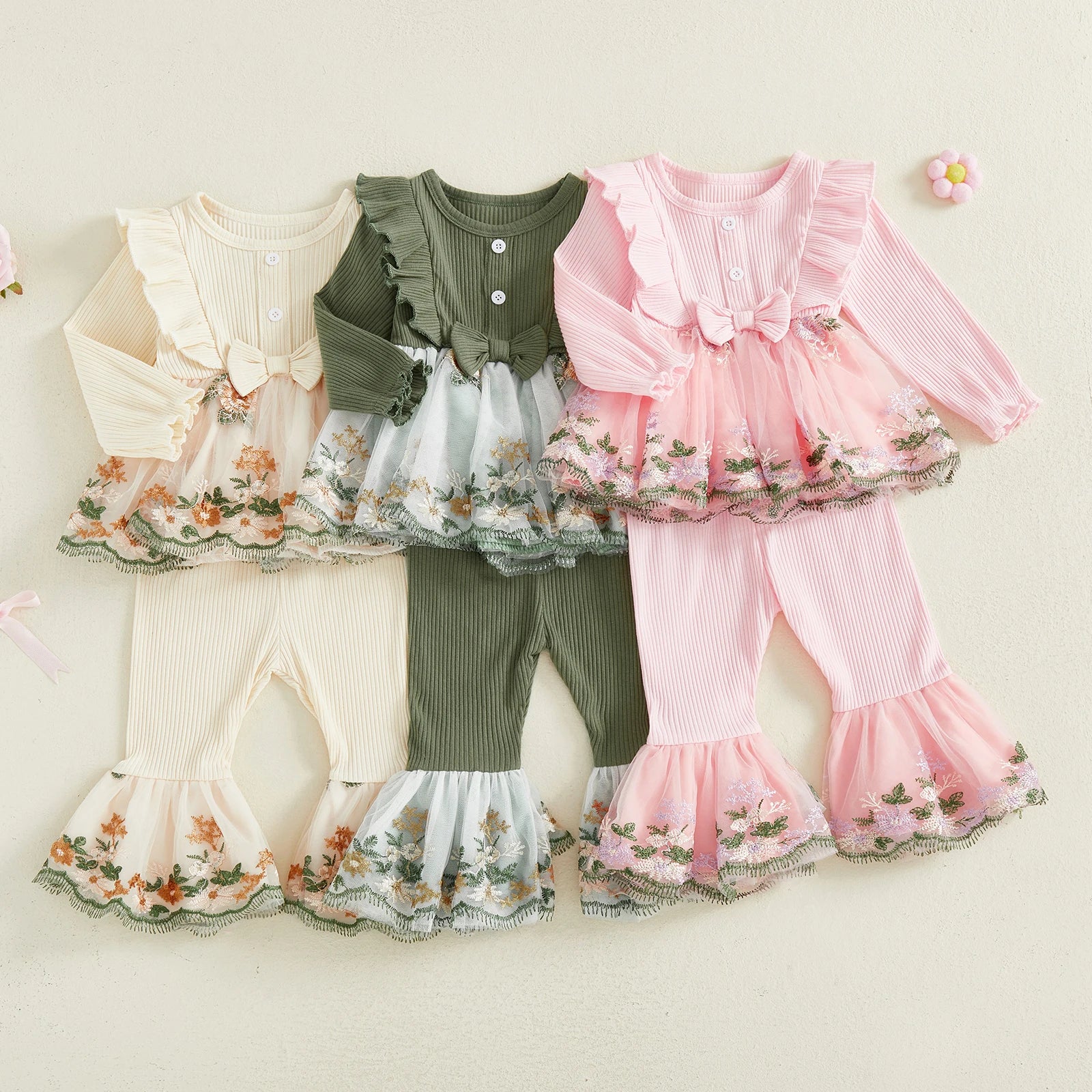 Three children's outfits in beige, green, and pink with floral details on a light background