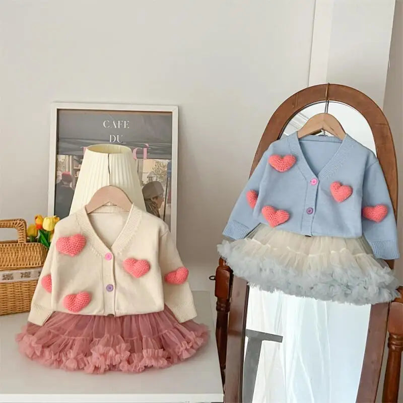 Children's clothing with heart details on hangers against a neutral background