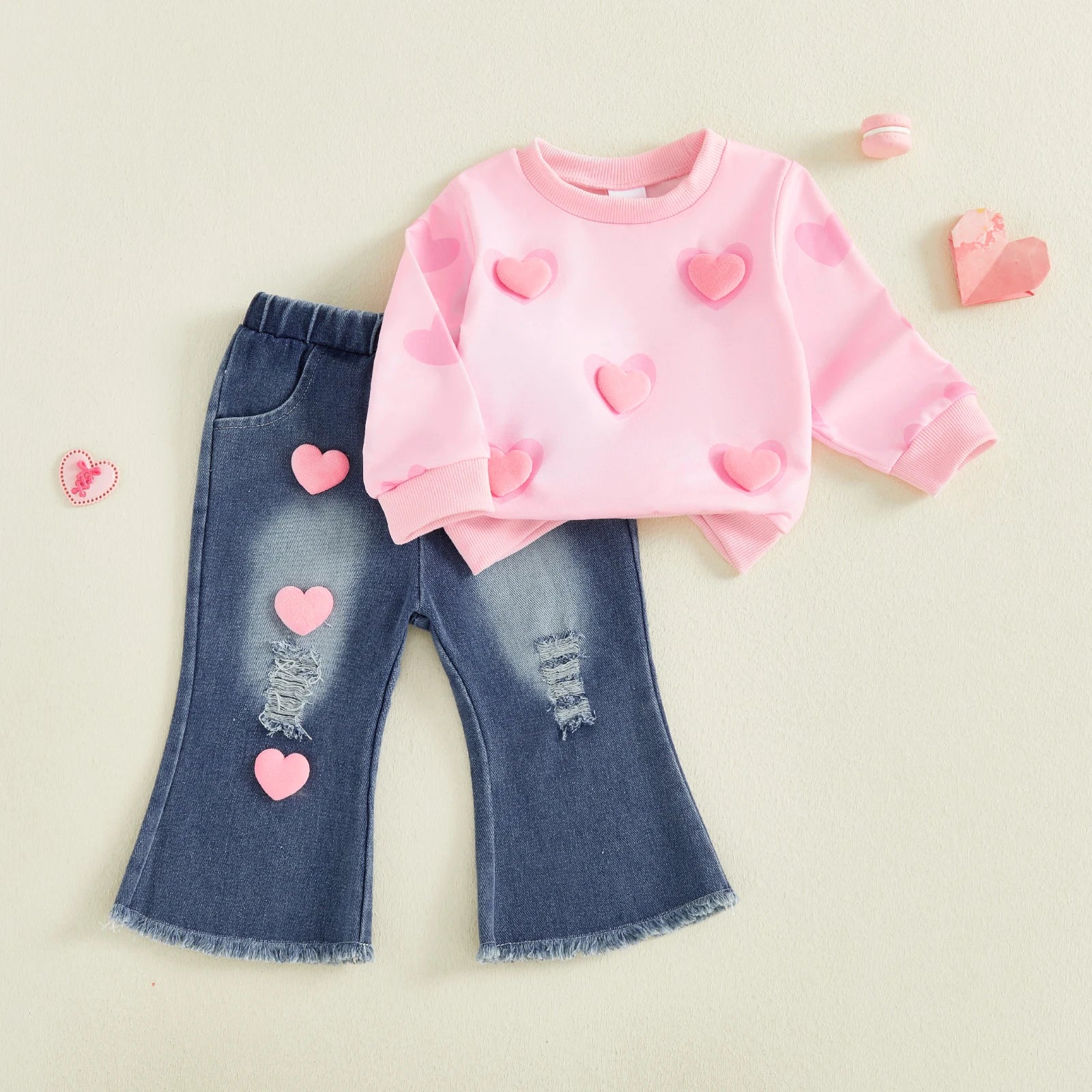 Pink sweatshirt and blue jeans with heart patterns on a light beige background