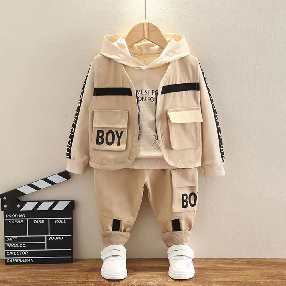 Children's beige outfit with 'BOY' text on a wooden floor and beige wall background