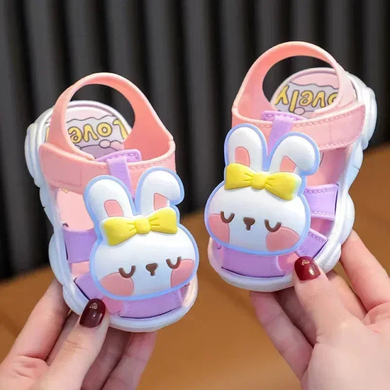 Pair of cartoon rabbit sandals held by a person against a dark background