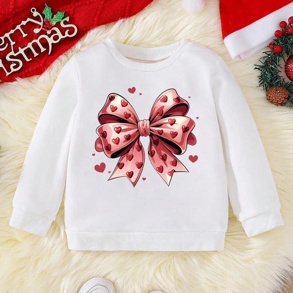 White sweater with a pink bow design on a textured surface with Christmas decorations.