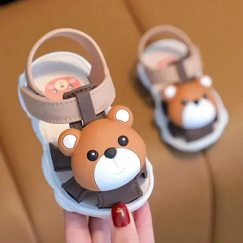 Children's sandals with bear design held by a hand against a brown background