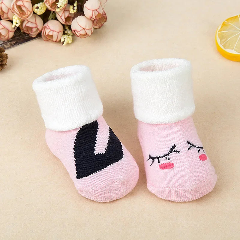 Pair of pink baby socks with face design on a beige background