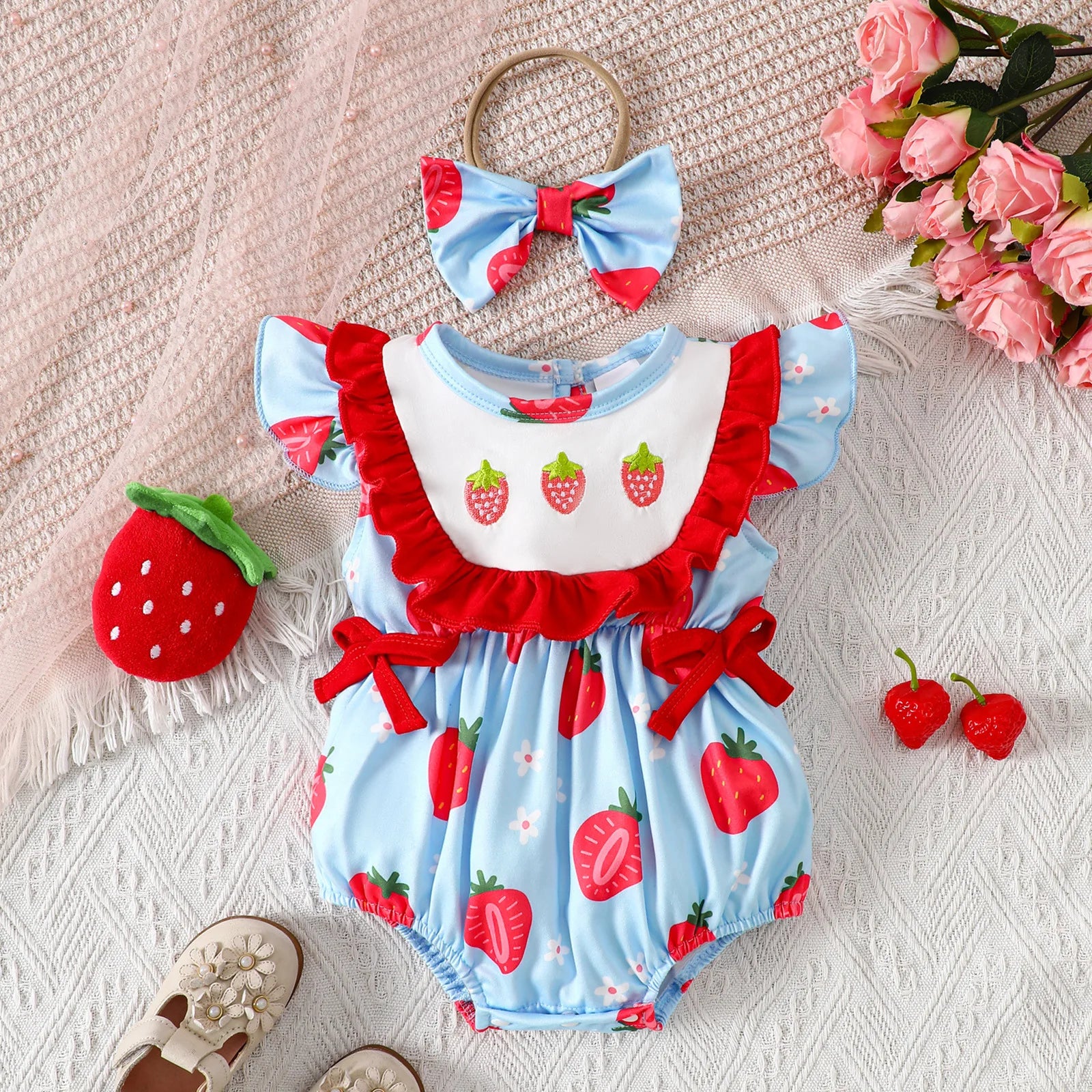 Baby romper with strawberry pattern, headband, and accessories on a textured surface.