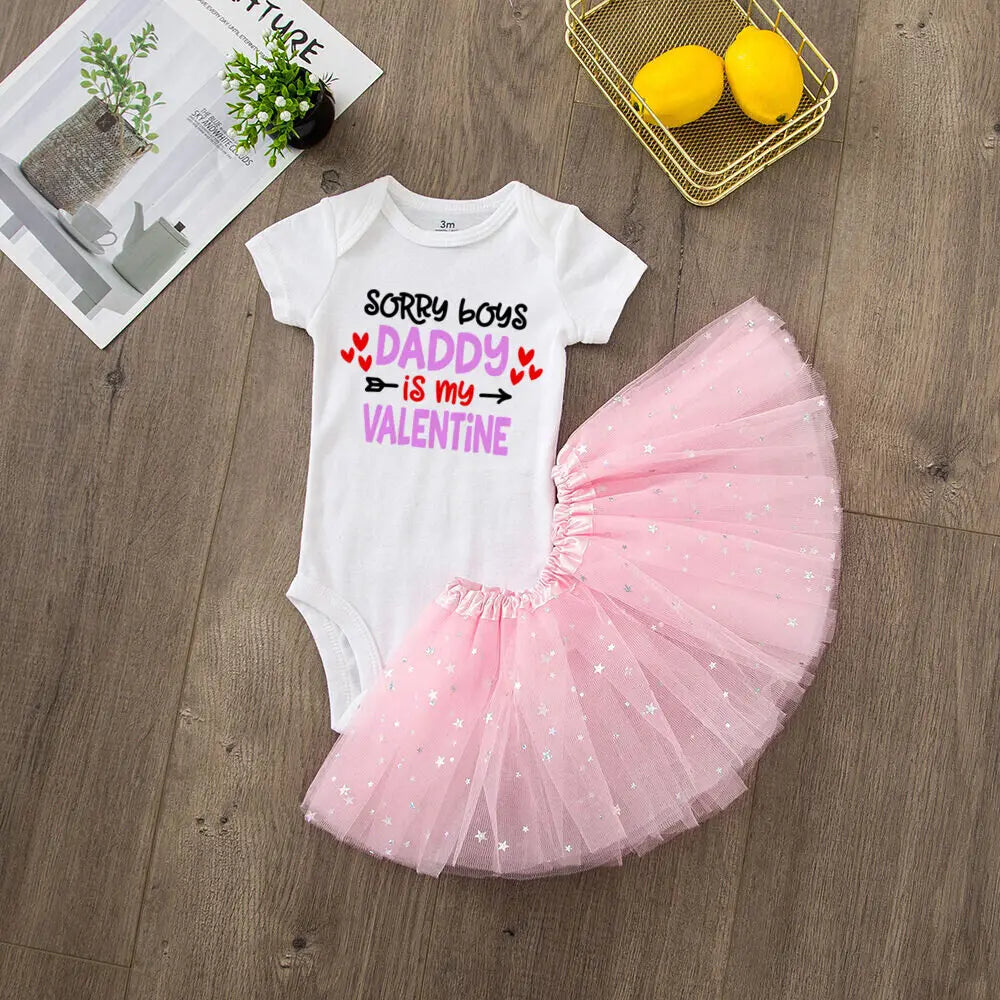 Baby outfit with pink tutu and text on a wooden surface