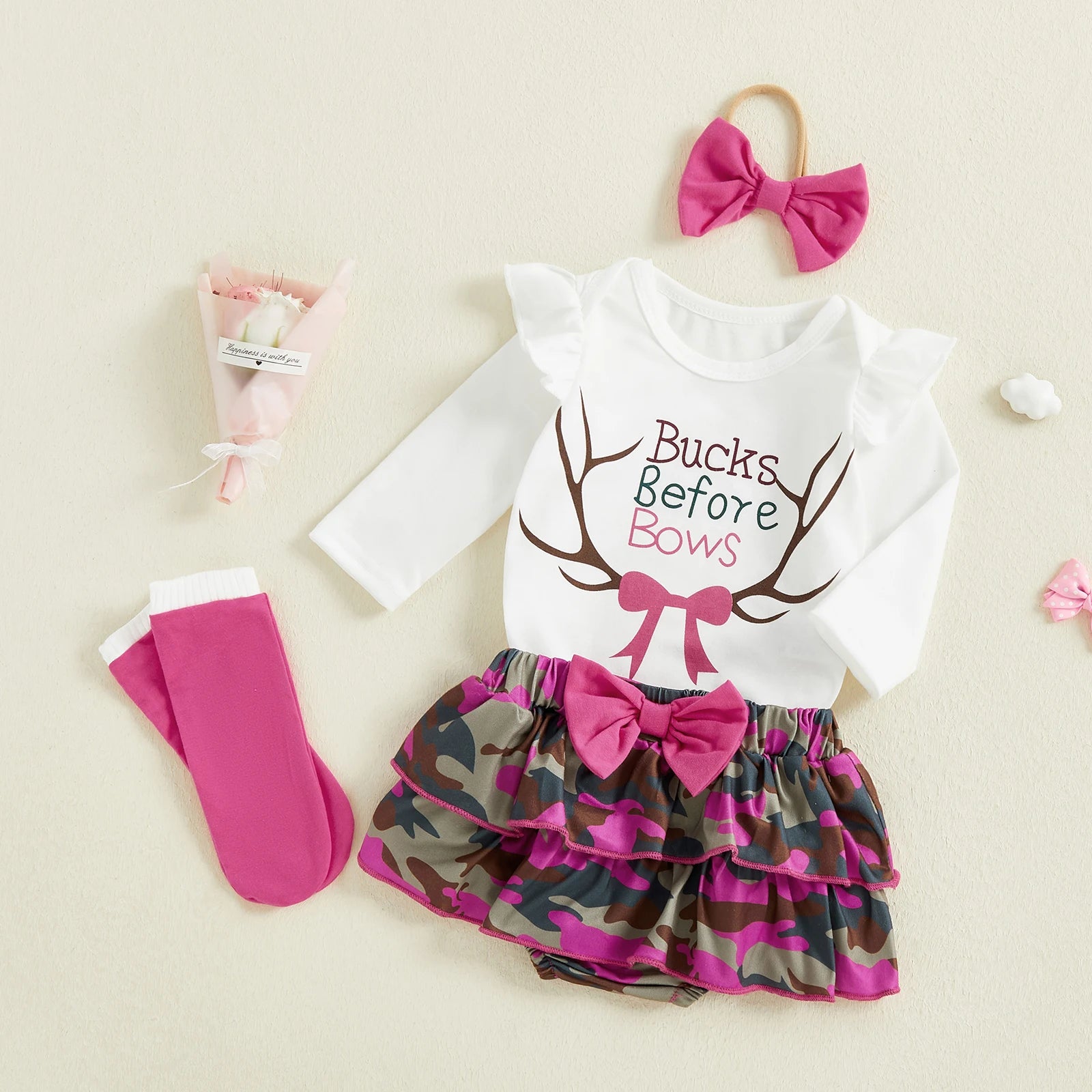Baby outfit set with white long-sleeve top, camo skirt, pink socks, and headband on a beige background.