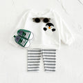 Children's outfit with white shirt featuring a penguin design, striped pants, and green shoes on a light gray background.