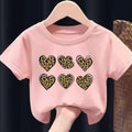 Pink t-shirt with leopard print heart designs on a hanger against a dark background