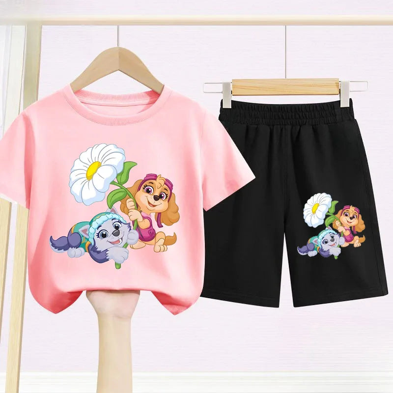 Children's pink t-shirt and black shorts with cartoon character design on hangers against a white background.