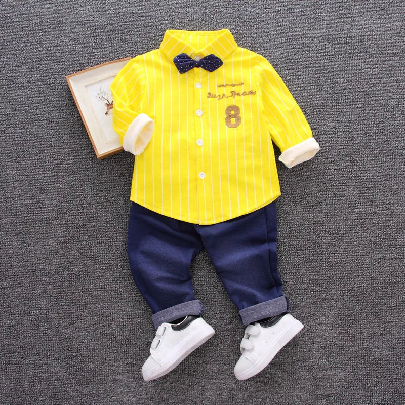 Children's outfit with yellow shirt, navy pants, and white shoes on a gray background