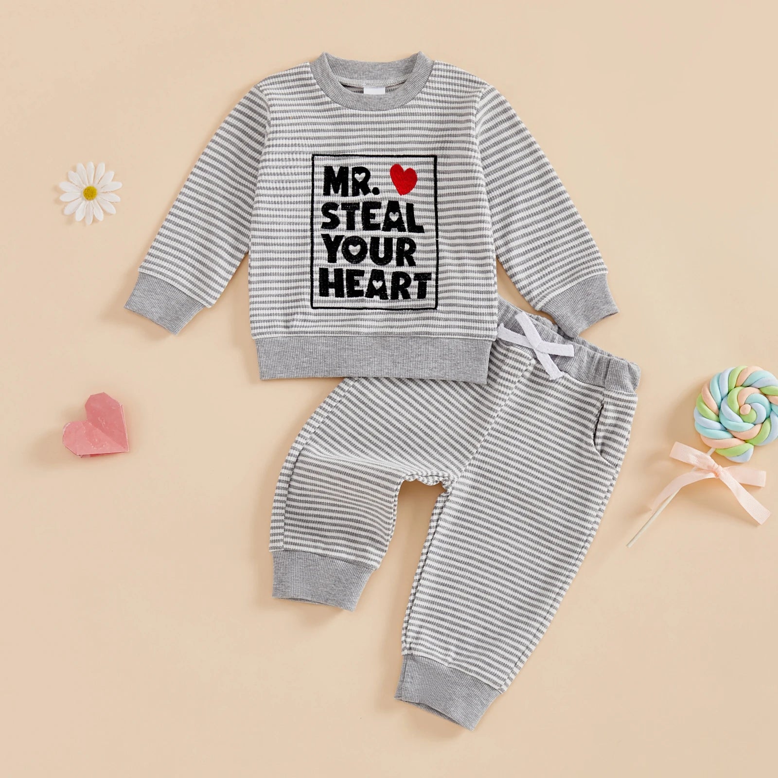 Children's striped outfit with text and heart graphic on a beige background