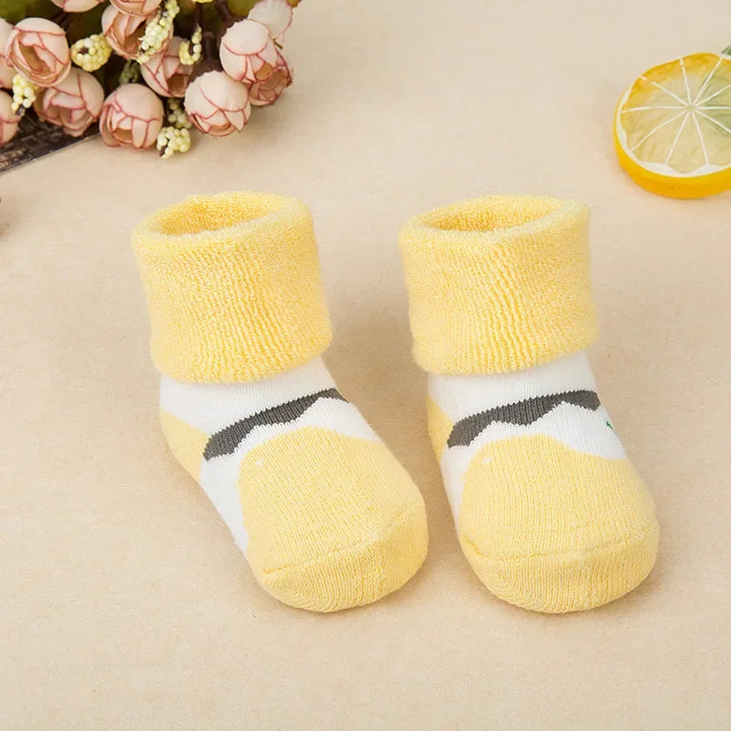 Pair of yellow baby socks with striped cuffs on a beige surface.