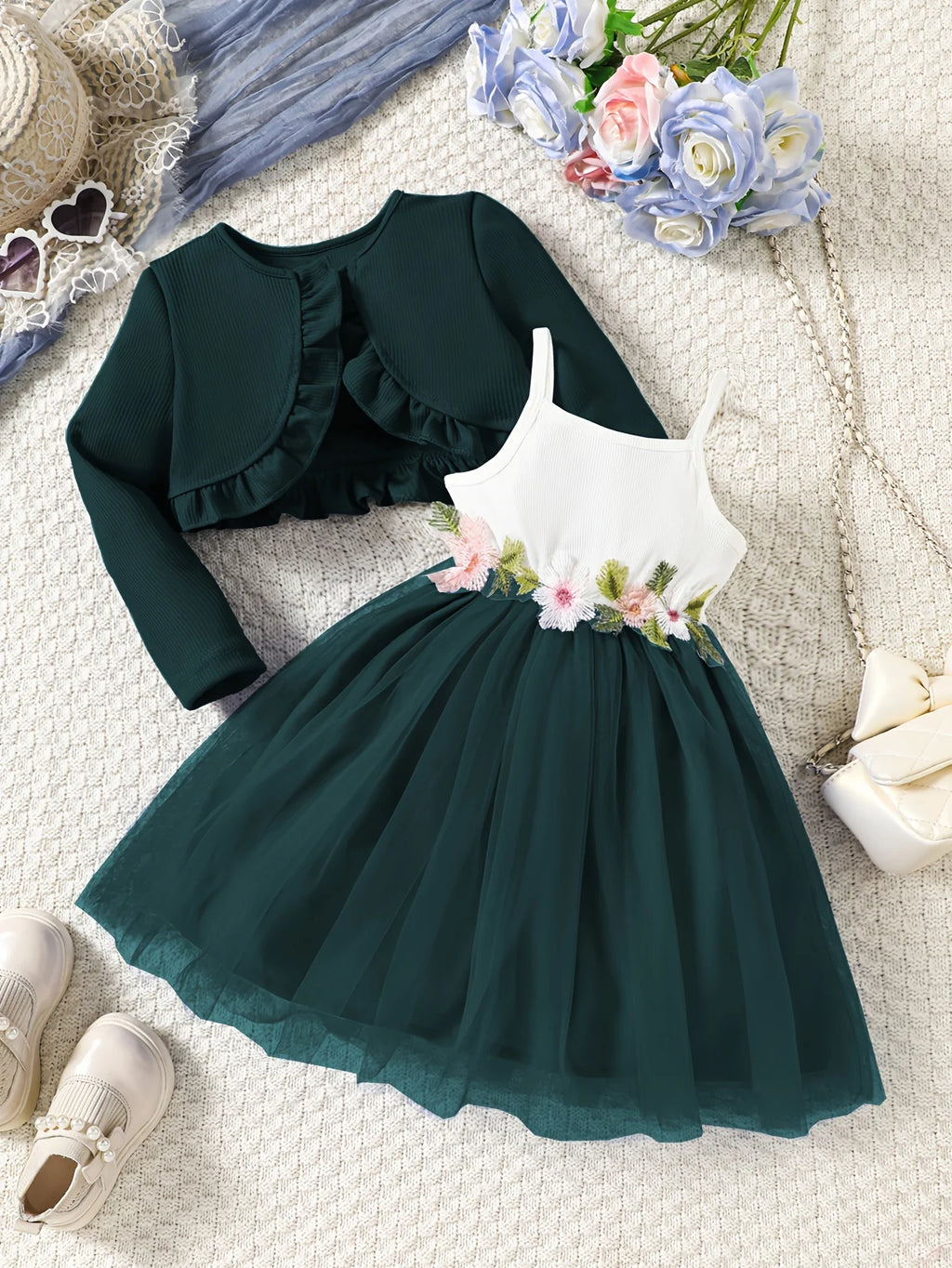 Green dress with floral details and matching bolero on a textured surface with flowers and shoes.