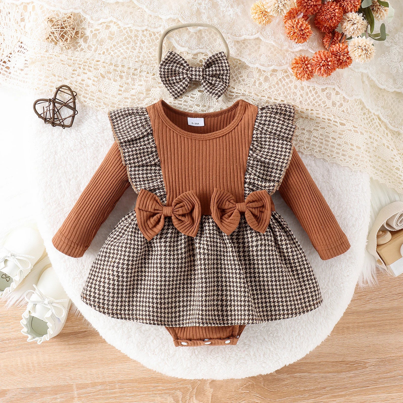 Baby outfit with brown and plaid dress, headband, and bloomers on a decorative background.